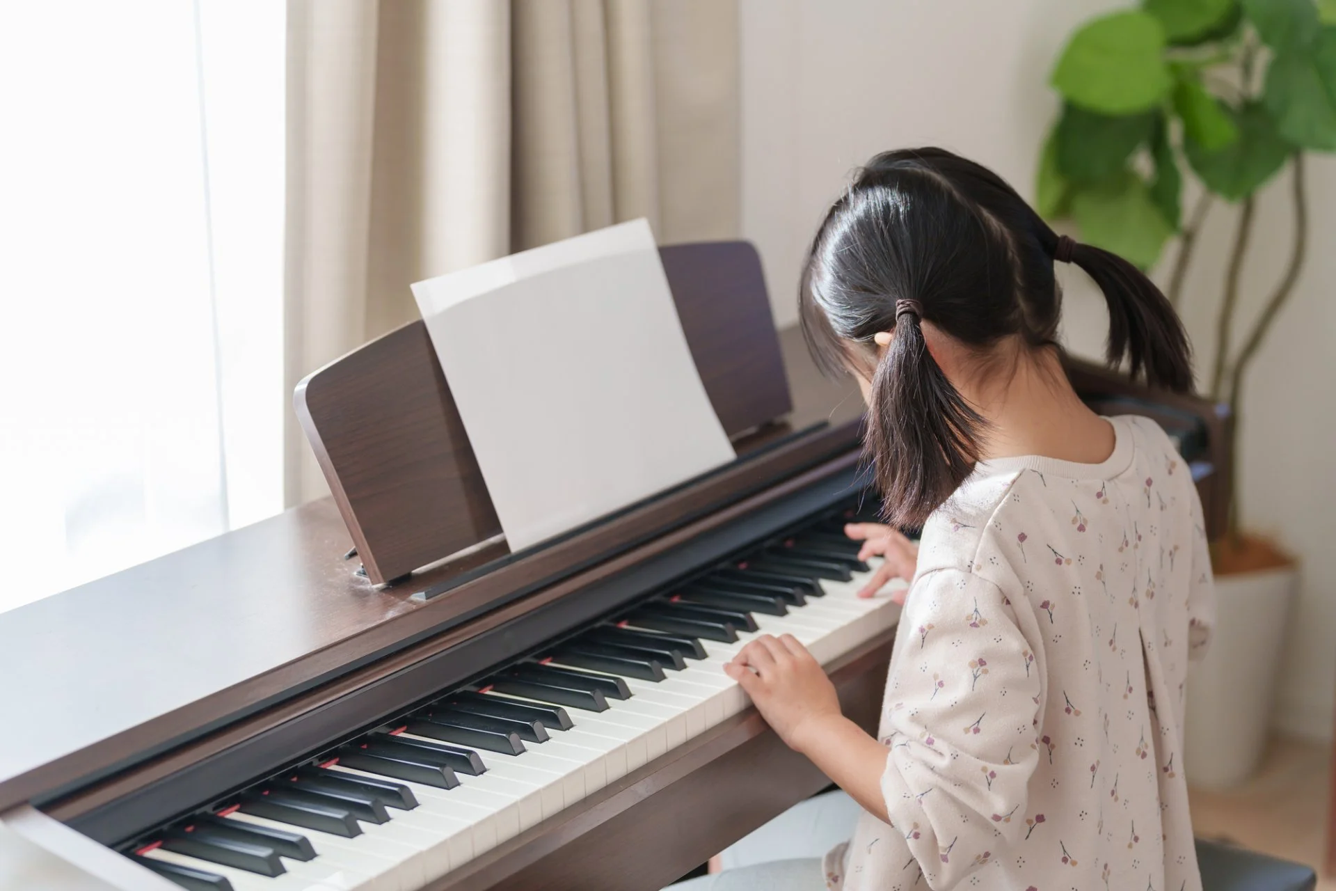 教室のピアノのそばで子どもが先生と向かい合い、笑顔で手を動かしているレッスン風景