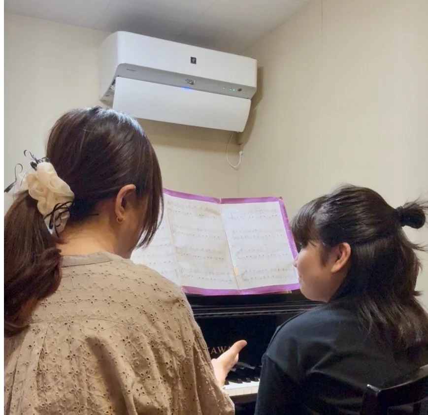 発表会の会場で子どもがピアノに向かい、客席の前で演奏の準備をしている後ろ姿