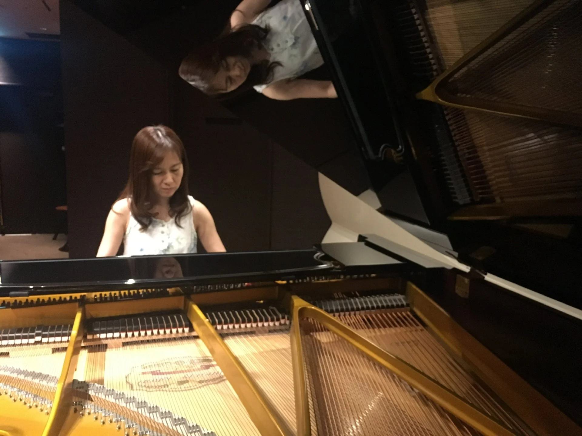 グランドピアノを演奏する先生と、ピアノの屋根に映り込む姿