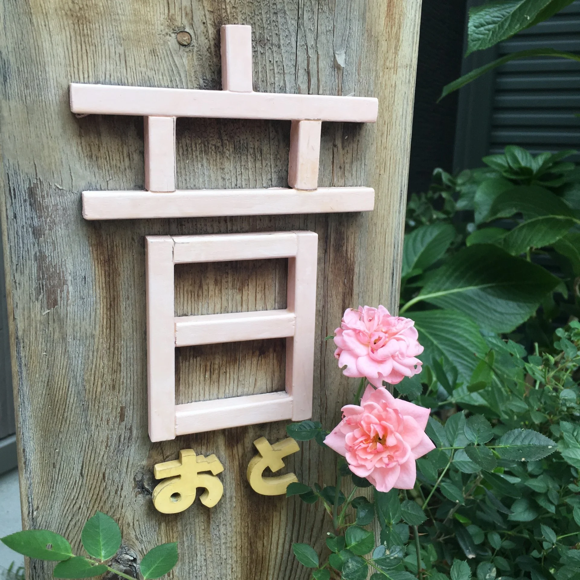 木の看板に付けられたピンク色の「音」の文字と、そばに咲くピンクのバラ